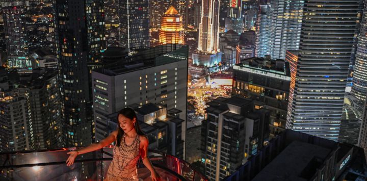 Una mujer posa para una foto con el horizonte nocturno de fondo en Kuala Lumpur, Malasia.