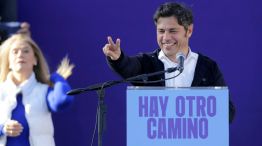Kicillof saluda, sonriente, con Magario de fondo.