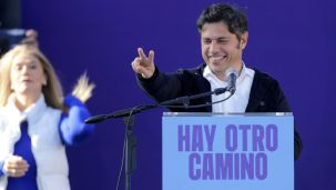 Kicillof saluda, sonriente, con Magario de fondo.