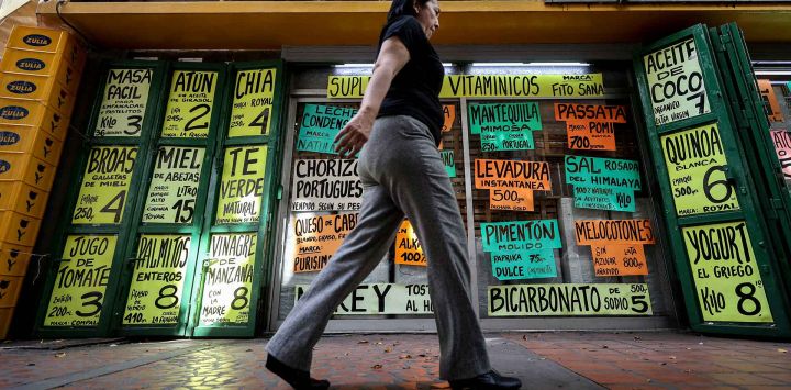Una mujer pasa junto a carteles con precios en dólares estadounidenses en Caracas, Venezuela. Foto de Pedro MATTEY / AFP