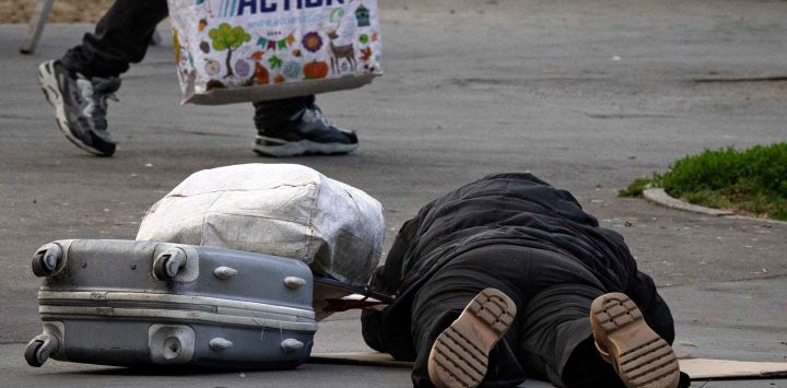 Un hombre sin hogar yace en una acera junto a sus pertenencias en París. Foto de JOEL SAGET / AFP