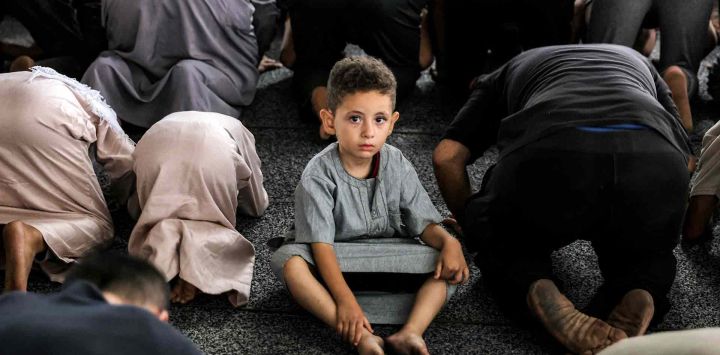 Un niño observa sentado entre los fieles musulmanes que se postran mientras realizan las oraciones matutinas del Eid al-Adha. Foto de Bashar TALEB / AFP