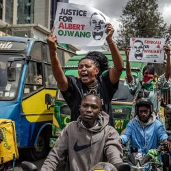 Manifestantes portan pancartas y corean consignas mientras gesticulan contra la policía mientras conducen motocicletas e intentan bloquear el tráfico en una carretera principal durante una marcha por la muerte del bloguero keniano Albert Ojwang, quien falleció bajo custodia policial en circunstancias controvertidas, en Nairobi. | Foto:LUIS TATO / AFP