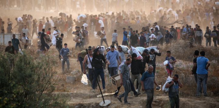 Personas transportan suministros de la Fundación Humanitaria de Gaza (FGH), un grupo de ayuda privado respaldado por Estados Unidos que ha eludido el sistema de la ONU en el territorio, mientras palestinos desplazados regresan de un centro de distribución de ayuda en el centro de la Franja de Gaza. La ONU y las principales organizaciones de ayuda se han negado a cooperar con la FGH, alegando la preocupación de que estuviera diseñada para atender objetivos militares israelíes.