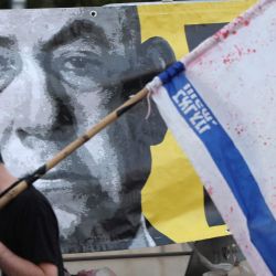 Un manifestante con la bandera israelí pasa junto a un retrato del primer ministro Benjamin Netanyahu durante una protesta antigubernamental que exige la liberación de los rehenes israelíes cautivos desde los ataques del 7 de octubre de 2023 perpetrados por militantes palestinos. Esta protesta se llevó a cabo frente al Ministerio de Defensa en Tel Aviv, en medio de la guerra en curso contra el movimiento militante palestino Hamás. | Foto:JACK GUEZ / AFP