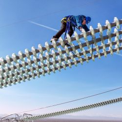 Vista aérea tomada con un dron de un trabajador operando sobre los cables del proyecto de transmisión de corriente continua de ultra alta tensión de ±800 kV Hami-Chongqing, en Hami, en la región autónoma uygur de Xinjiang, en el noroeste de China. | Foto:Xinhua/Ma Yuan