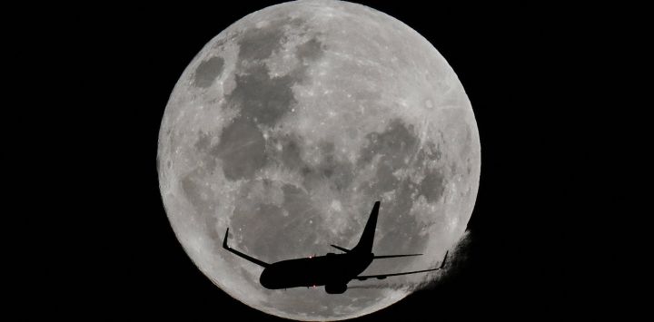 Un avión pasa frente a la luna llena, conocida como "Luna de Fresa", sobre la playa de Coogee en Sídney, Australia.