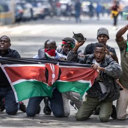 Manifestantes portan una bandera keniana mientras se protegen de los gases lacrimógenos y las balas de goma durante los enfrentamientos entre manifestantes y policías durante una protesta por la muerte del bloguero keniano Albert Ojwang, quien falleció bajo custodia policial, mientras el gobierno presenta el presupuesto 2025-2026 en el centro de Nairobi. | Foto:LUIS TATO / AFP