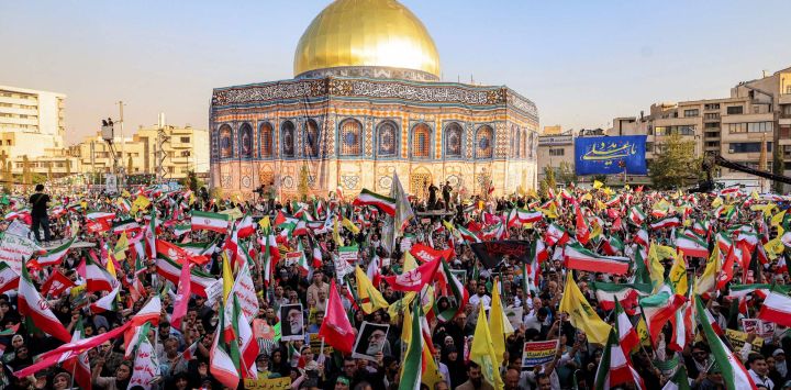 Manifestantes ondean banderas amarillas del Hezbolá libanés y de Irán frente a una réplica del Santuario de la Cúpula de la Roca de Jerusalén durante una manifestación en solidaridad con el gobierno contra los ataques de Israel a Irán y para conmemorar el Eid al-Ghadir, fecha en la que, según la creencia chiita, el profeta Mahoma designó a su sobrino y compañero Ali ibn Abi Talib como su sucesor. Esta manifestación se llevó a cabo en la plaza Enghelab de Teherán.