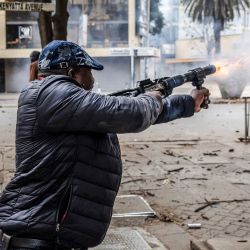 Un agente de la Policía de Kenia, vestido de civil, dispara una bomba de gas lacrimógeno mientras estallan enfrentamientos durante una manifestación por la muerte del bloguero keniano Albert Ojwang, quien falleció bajo custodia policial, en el centro de Nairobi. | Foto:LUIS TATO / AFP