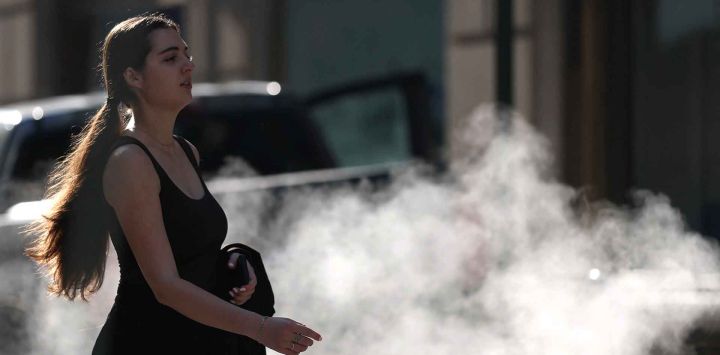 Una mujer pasa junto a una rejilla de vapor en Wall Street, mientras se emite una alerta de calor extremo para el área de Nueva York. Foto de TIMOTHY A. CLARY / AFP