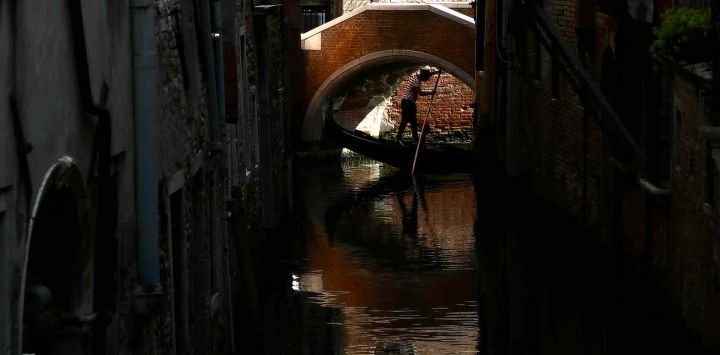 Un gondolero maniobra su góndola bajo un pequeño puente en la laguna de Venecia. Foto de Marco BERTORELLO / AFP