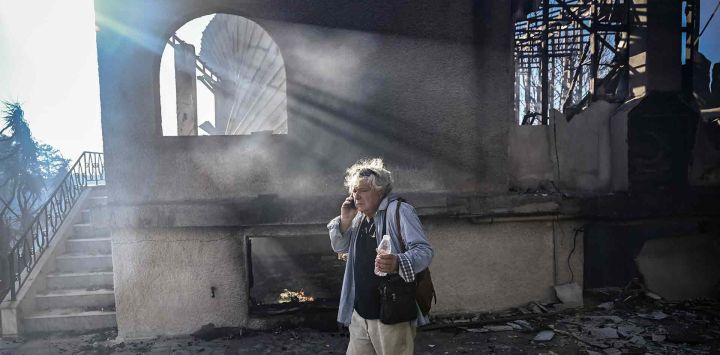 Un hombre habla por teléfono junto a una casa quemada tras un incendio forestal en Thymari, al sureste de Atenas. Foto de Aris MESSINIS / AFP