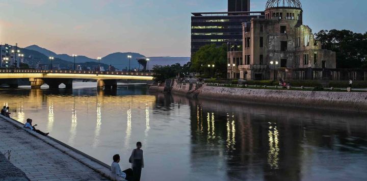 Vista general muestra a personas sentadas junto al río frente a la Cúpula de la Bomba Atómica en Hiroshima. Foto de Richard A. Brooks / AFP