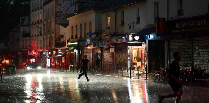 La gente corre a refugiarse en una calle del distrito 20 durante una tormenta eléctrica, en París. Foto de Christophe DELATTRE / AFP