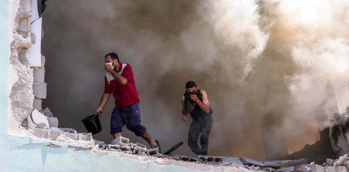 Hombres se cubren el rostro mientras se elevan columnas de humo tras un ataque israelí en la escuela Osama bin Zaid de la UNRWA en el distrito de Saftawi. Foto de Bashar TALEB / AFP