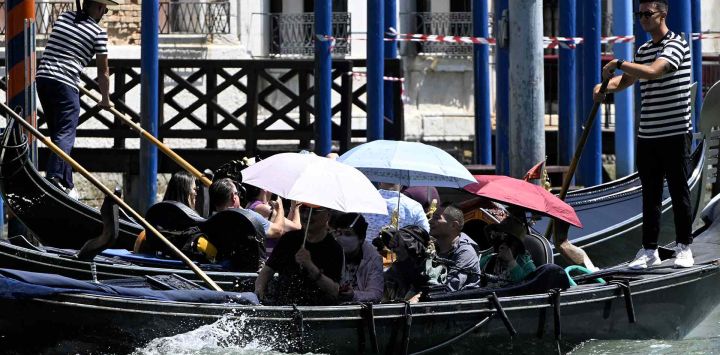 Turistas se protegen del sol con sombrillas durante un paseo en góndola por la laguna de Venecia. Foto de ANDREA PATTARO / AFP