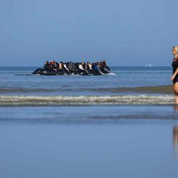 Turistas caminan por la orilla mientras migrantes abordan un barco de contrabandistas en un intento de cruzar el Canal de la Mancha. Foto de Sameer Al-DOUMY / AFP | Foto:AFP