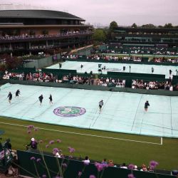 Los miembros del personal de campo retiran la cubierta protectora de la cancha en el Campeonato de Wimbledon 2025, en Londres. Foto de HENRY NICHOLLS / AFP | Foto:AFP