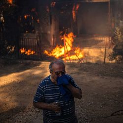 Un hombre se encuentra frente a una casa en llamas durante un incendio forestal en Pikermi, Atenas. Foto de Angelos TZORTZINIS / AFP | Foto:AFP