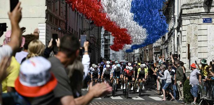 El pelotón circula bajo banderines decorativos colgados sobre el recorrido de la carrera en Aire-sur-la-Lys durante la tercera etapa de la 112ª edición del Tour de Francia, 178,3 km entre Valenciennes y Dunkerque (Dunkerque), en el norte de Francia.