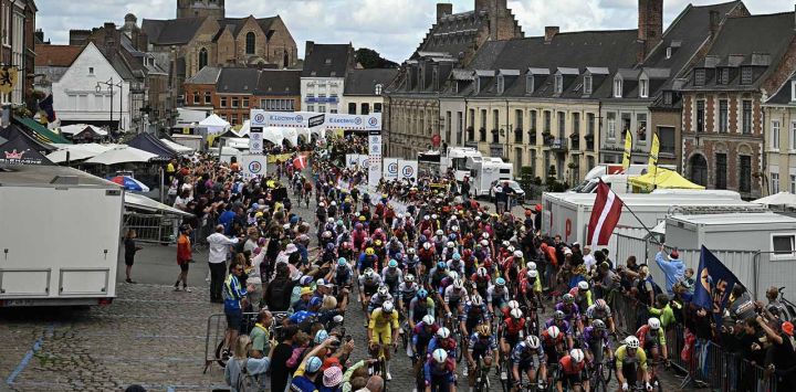 El pelotón circula bajo banderines decorativos colgados sobre el recorrido de la carrera en Aire-sur-la-Lys durante la tercera etapa de la 112ª edición del Tour de Francia, 178,3 km entre Valenciennes y Dunkerque (Dunkerque), en el norte de Francia.