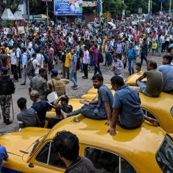 Los taxistas observan a los manifestantes gritar consignas mientras marchan hacia el edificio de la Secretaría de Estado, exigiendo la reincorporación laboral de los docentes elegibles cuyos empleos fueron anulados por orden de la Corte Suprema, en Howrah, a las afueras de Calcuta, India. | Foto:DIBYANGSHU SARKAR / AFP