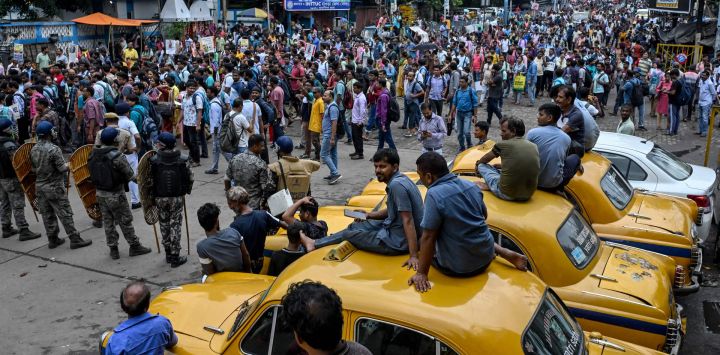 Los taxistas observan a los manifestantes gritar consignas mientras marchan hacia el edificio de la Secretaría de Estado, exigiendo la reincorporación laboral de los docentes elegibles cuyos empleos fueron anulados por orden de la Corte Suprema, en Howrah, a las afueras de Calcuta, India.