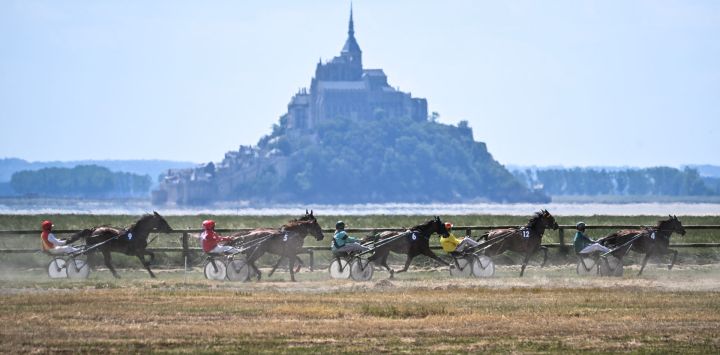Caballos cabalgan por el hipódromo de Genet, con el Mont-Saint-Michel al fondo, para celebrar su 130.º aniversario, en Genet, noroeste de Francia.