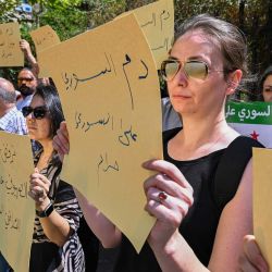 Sirios levantan pancartas mientras se manifiestan en protesta por los enfrentamientos sectarios y los ataques israelíes frente al parlamento en Damasco. | Foto:LOUAI BESHARA / AFP