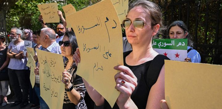 Sirios levantan pancartas mientras se manifiestan en protesta por los enfrentamientos sectarios y los ataques israelíes frente al parlamento en Damasco.