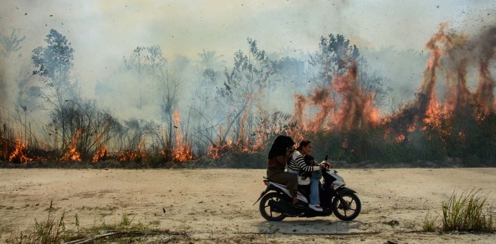 Personas en moto pasan junto a un incendio forestal en Karya Indah, provincia de Riau, Indonesia.