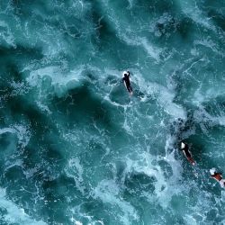 Esta fotografía aérea muestra a surfistas nadando entre las olas en sus tablas de surf junto al Océano Atlántico en Carcans, suroeste de Francia. | Foto:Christophe Archambault / AFP