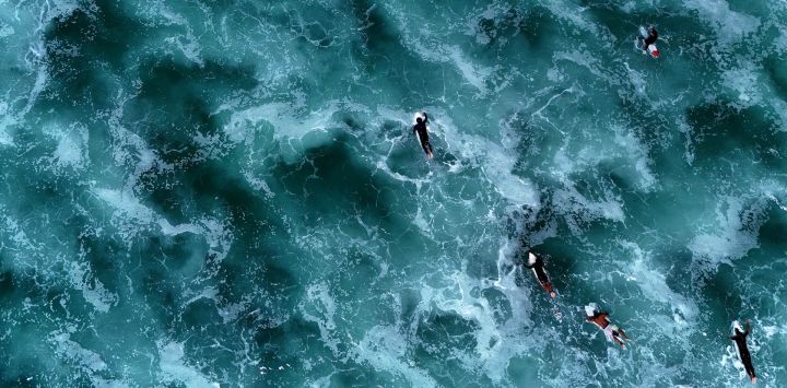 Esta fotografía aérea muestra a surfistas nadando entre las olas en sus tablas de surf junto al Océano Atlántico en Carcans, suroeste de Francia.