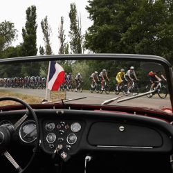 El ciclista esloveno Tadej Pogacar, del equipo UAE Team Emirates - XRG, luciendo el maillot amarillo de líder de la general, pedalea con el pelotón junto a un coche clásico aparcado en el recorrido durante la 17.ª etapa de la 112.ª edición del Tour de Francia, de 160,4 km entre Bolléne y Valence, en el sur de Francia. | Foto:ANNE-CHRISTINE POUJOULAT / AFP