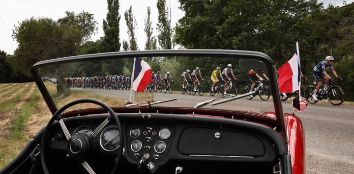 El ciclista esloveno Tadej Pogacar, del equipo UAE Team Emirates - XRG, luciendo el maillot amarillo de líder de la general, pedalea con el pelotón junto a un coche clásico aparcado en el recorrido durante la 17.ª etapa de la 112.ª edición del Tour de Francia, de 160,4 km entre Bolléne y Valence, en el sur de Francia.