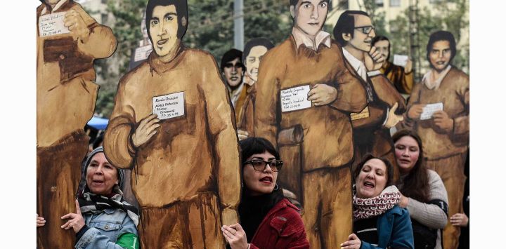 Personas participan en una manifestación en conmemoración de los 50 años de Operación Colombo mientras sostienen fotografías de personas detenidas y desaparecidas, en Santiago, capital de Chile.