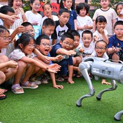 Imagen de niños interactuando con un perro robótico, en la ciudad de Meishan, en la provincia de Sichuan, en el suroeste de China. Niños participan en diversas actividades durante las vacaciones de verano en todo el país. | Foto:Xinhua/Pan Jianyong