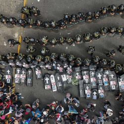 Vista aérea de familiares de víctimas de protestas portando ataúdes negros y fotografías de sus seres queridos fallecidos frente a la policía antidisturbios durante una protesta contra el gobierno de la presidenta Dina Boluarte en Lima. | Foto:CONNIE FRANCE / AFP
