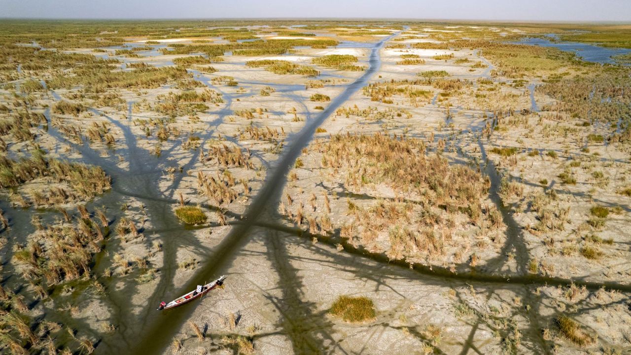 Una imagen aérea muestra a lugareños descansando junto a una barca tradicional en uno de los canales creados por la retirada de las aguas de las marismas de Chibayish, afectadas por la sequía, en la provincia de Dhi Qar, al sur de Irak. Los 46 millones de iraquíes se enfrentan al aumento de las temperaturas, la escasez crónica de agua y sequías anuales, en un país intensamente afectado por los efectos del cambio climático. | Foto:ASAAD NIAZI / AFP