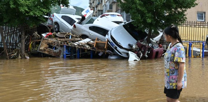 Una mujer camina junto a vehículos dañados en un barrio inundado del distrito de Miyun, al norte de Pekín. Las fuertes lluvias en Pekín causaron la muerte de 30 personas y obligaron a las autoridades a evacuar a decenas de miles de personas mientras zonas del norte de China eran azotadas por aguaceros torrenciales que provocaron deslizamientos de tierra mortales, según informaron medios estatales.