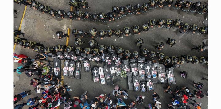 Vista aérea de familiares de víctimas de protestas portando ataúdes negros y fotografías de sus seres queridos fallecidos frente a la policía antidisturbios durante una protesta contra el gobierno de la presidenta Dina Boluarte en Lima.
