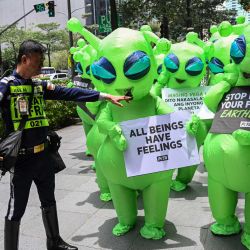 Un guardia de seguridad hace un gesto a personas que visten disfraces de extraterrestres, durante una protesta en el distrito financiero de Manila, como parte de su campaña para promover una alimentación vegana y denunciar las emisiones de gases de efecto invernadero de la agricultura. | Foto:TED ALJIBE / AFP