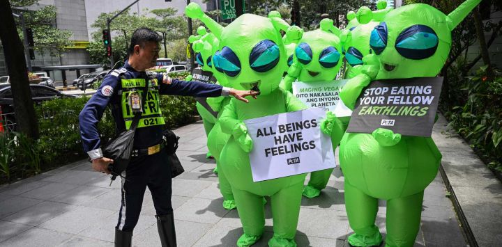 Un guardia de seguridad hace un gesto a personas que visten disfraces de extraterrestres, durante una protesta en el distrito financiero de Manila, como parte de su campaña para promover una alimentación vegana y denunciar las emisiones de gases de efecto invernadero de la agricultura.