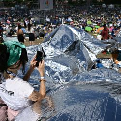 Una mujer usa su teléfono inteligente mientras jóvenes y peregrinos se reúnen en el barrio de Tor Vergata, al este de Roma, para una vigilia de oración dirigida por el Papa antes de la misa, en el marco del Jubileo de la Juventud. | Foto:Filippo Monteforte / AFP