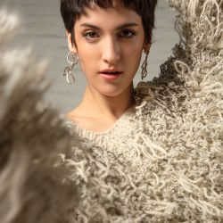 Suéter oversized cuello en V con flecos confeccionado con bouclé de lana de llama de color teñido natural (Maydi). Aros de plata y alpaca pulida (Limido Joyas).