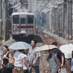 Se ve una neblina de calor al fondo mientras peatones con paraguas cruzan una vía férrea en un día caluroso en Tokio. | Foto:Kazuhiro Nogi / AFP