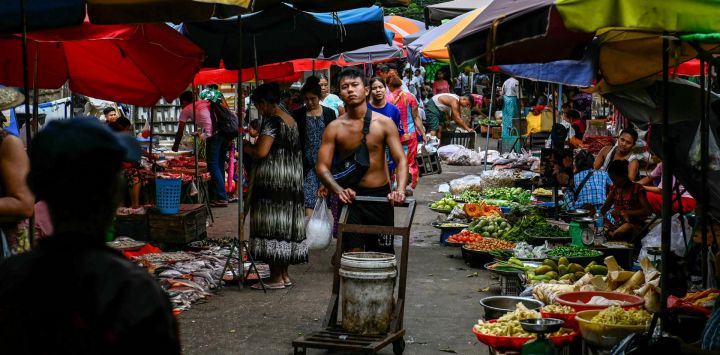 Un trabajador empuja un carrito junto a productos frescos en un mercado callejero de Yangon, Myanmar.