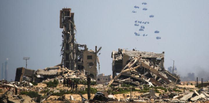 Palestinos observan el aterrizaje de paquetes de ayuda en paracaídas en la zona de Nuseirat, en el centro de la Franja de Gaza, durante un lanzamiento aéreo sobre el territorio palestino asediado por Israel.