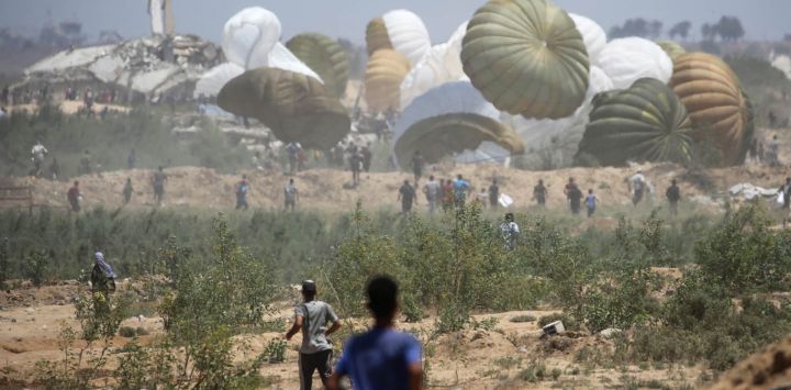 Palestinos acuden rápidamente al lugar donde aterrizan los paquetes de ayuda en paracaídas en la zona de Nuseirat, en el centro de la Franja de Gaza, durante un lanzamiento aéreo sobre el territorio palestino asediado por Israel.